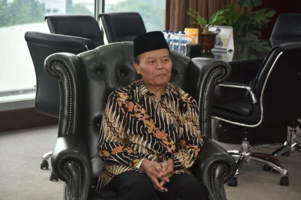 Indonesian official sitting in a black leather chair during a meeting.