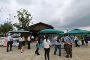 People gathering at Media Presisi booth during outdoor event.
